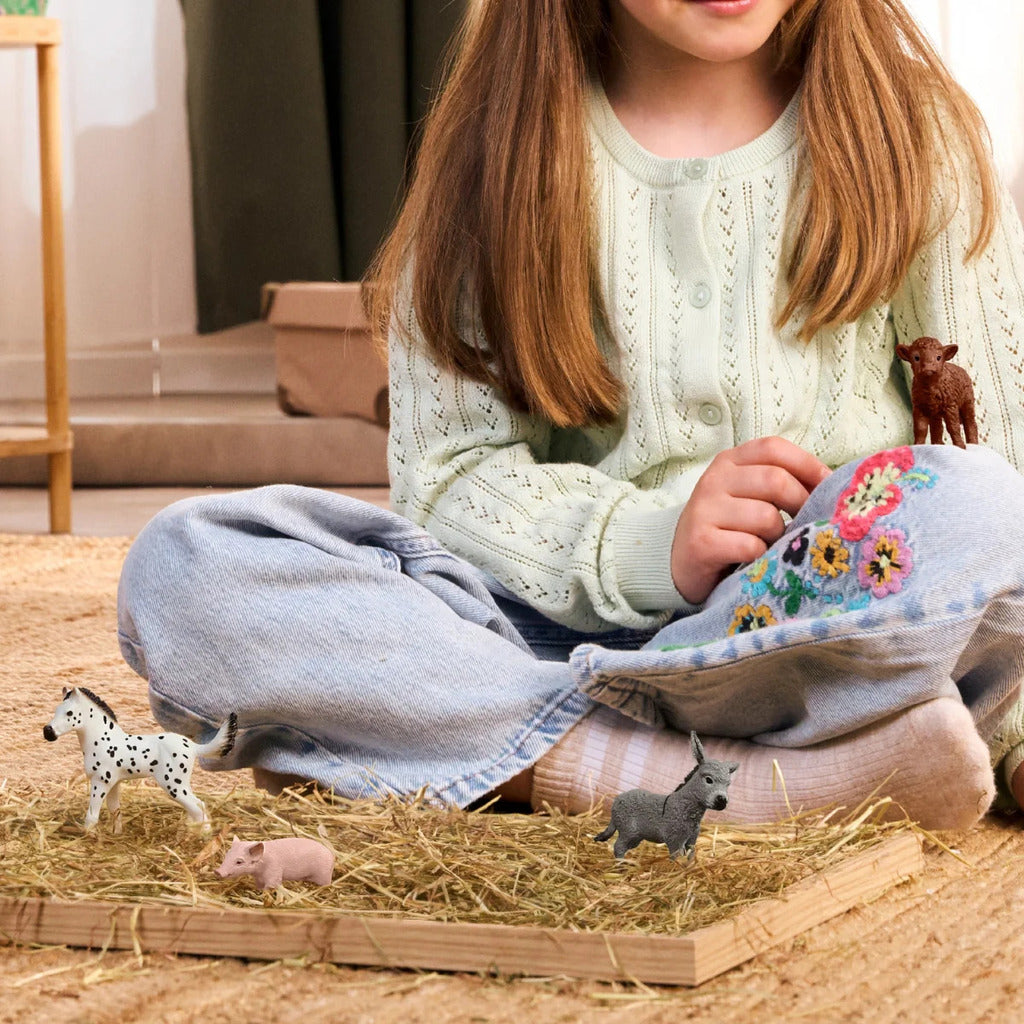 Child pairing Schleich baby farm animals with their adult counterparts on a play mat
