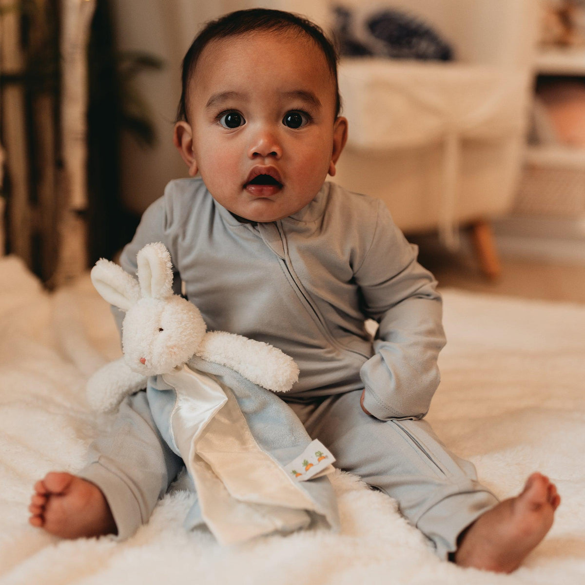 Baby in a blue onesie holding the Bud Bunny lovey
