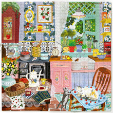 Completed jigsaw puzzle featuring a colourful country kitchen with pink cupboards, floral wallpaper, strawberry decorations, vintage stove, fresh bread, flowers and two cats beside a dining table.
