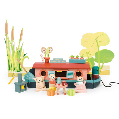 Tender Leaf Toys Little Otter Canal Boat arranged in an imaginative riverside play scene with three otter characters, miniature table, sleeping bags, fishing rod, stove, flowers and illustrated reeds and lily pads.