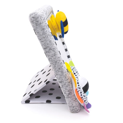 Side view of baby tummy time activity mirror showing the grey fabric frame, adjustable spotted kickstand, plush bee and colourful spinning flower toy.
