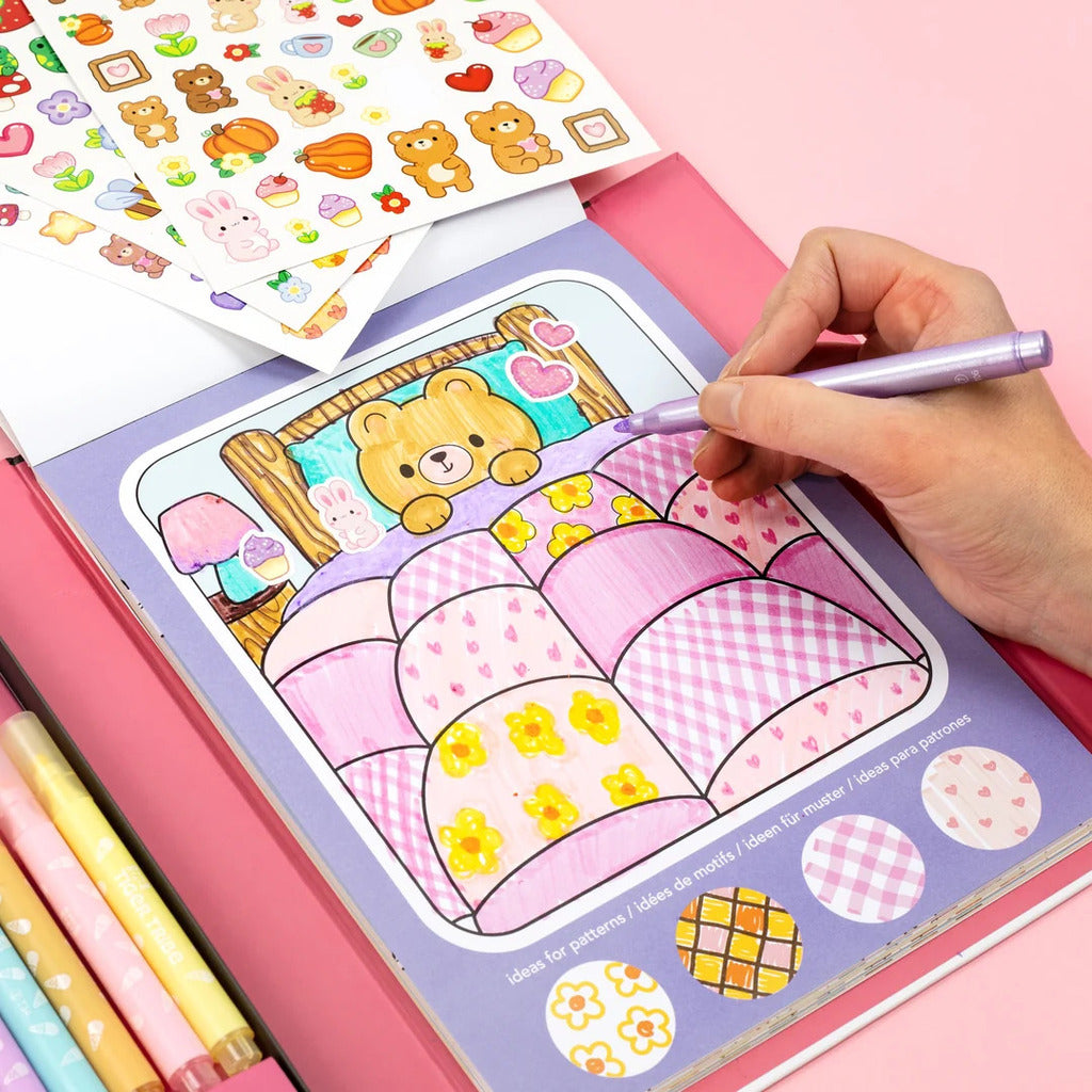 The colouring set open on a table with markers in use beside a partly finished illustrated page