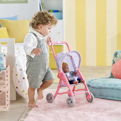Toddler pushing a Corolle baby doll in the flowered doll stroller across a smooth indoor floor