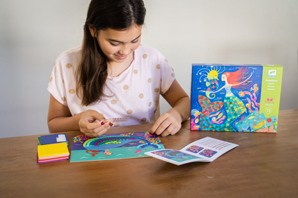 Child sticking foam squares onto a Djeco Mermaid's Song board during a calm craft activity
