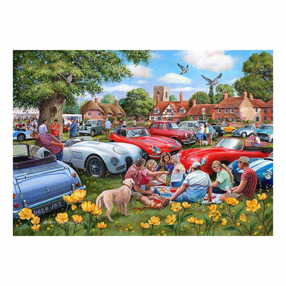 People enjoying a picnic by vintage cars in a village setting with flowers and trees.