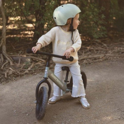 Child wearing a helmet seated on the Kinderfeets Trail Balance Bike in Silver Sage outdoors