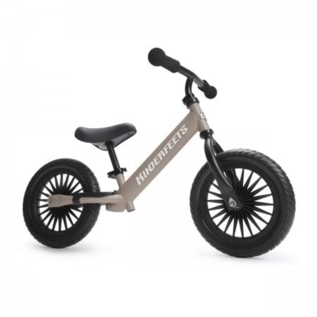 Kinderfeets children's balance bike in beige with black handlebars, adjustable saddle, footrest and two large black wheels, shown from the side.
