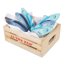 A wooden toy crate with the brand name 'LE TOY VAN' printed in red on the front, filled with blue and light blue fish-shaped wooden toys on a white background.