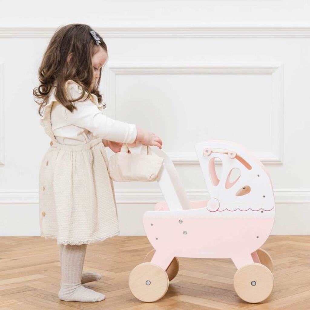Child pushing a doll in the Le Toy Van retro wooden doll pram, a toddler walking toy for ages 2 and up