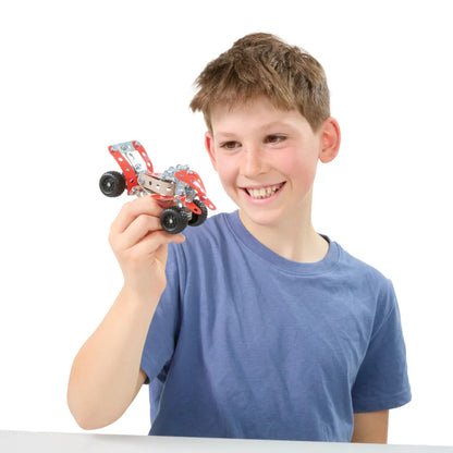 A smiling young boy with short brown hair, wearing a blue t-shirt, holds up a small red and gray toy race car with black wheels against a solid white background.