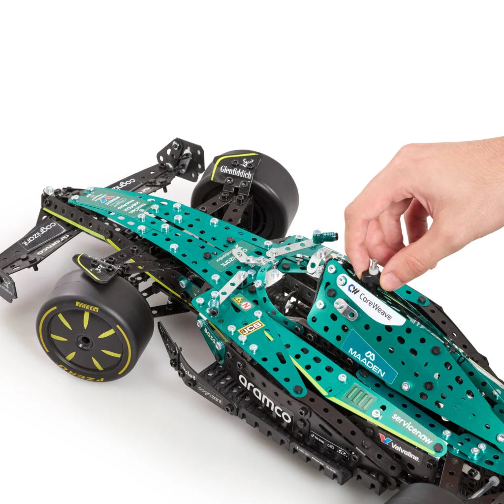 A hand is assembling a green and black toy Formula 1 car model, featuring visible sponsor decals like Mercedes, Castore, and Aramco, on a clean white background.