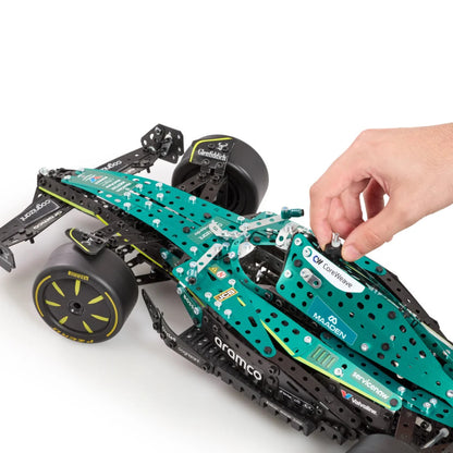 A hand is assembling a green and black toy Formula 1 car model, featuring visible sponsor decals like Mercedes, Castore, and Aramco, on a clean white background.