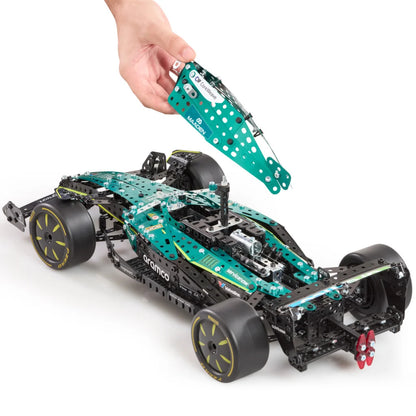 A hand holds a teal and white metal sheet above a partially assembled black and teal racing car model on a clean white background. The car has visible branding including 'Branco' and 'Mercedes'.
