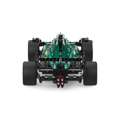 A high-angle view of a building block toy model representing an F1 race car chassis, featuring a green and black body with four black wheels, photographed on a solid white background.