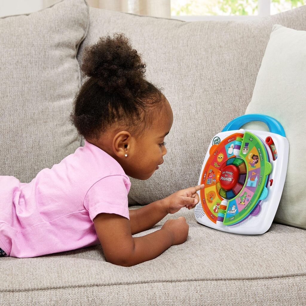 Toddler spinning the letter dial on the LeapFrog My 1st Phonics Spin & Learn toy at a table