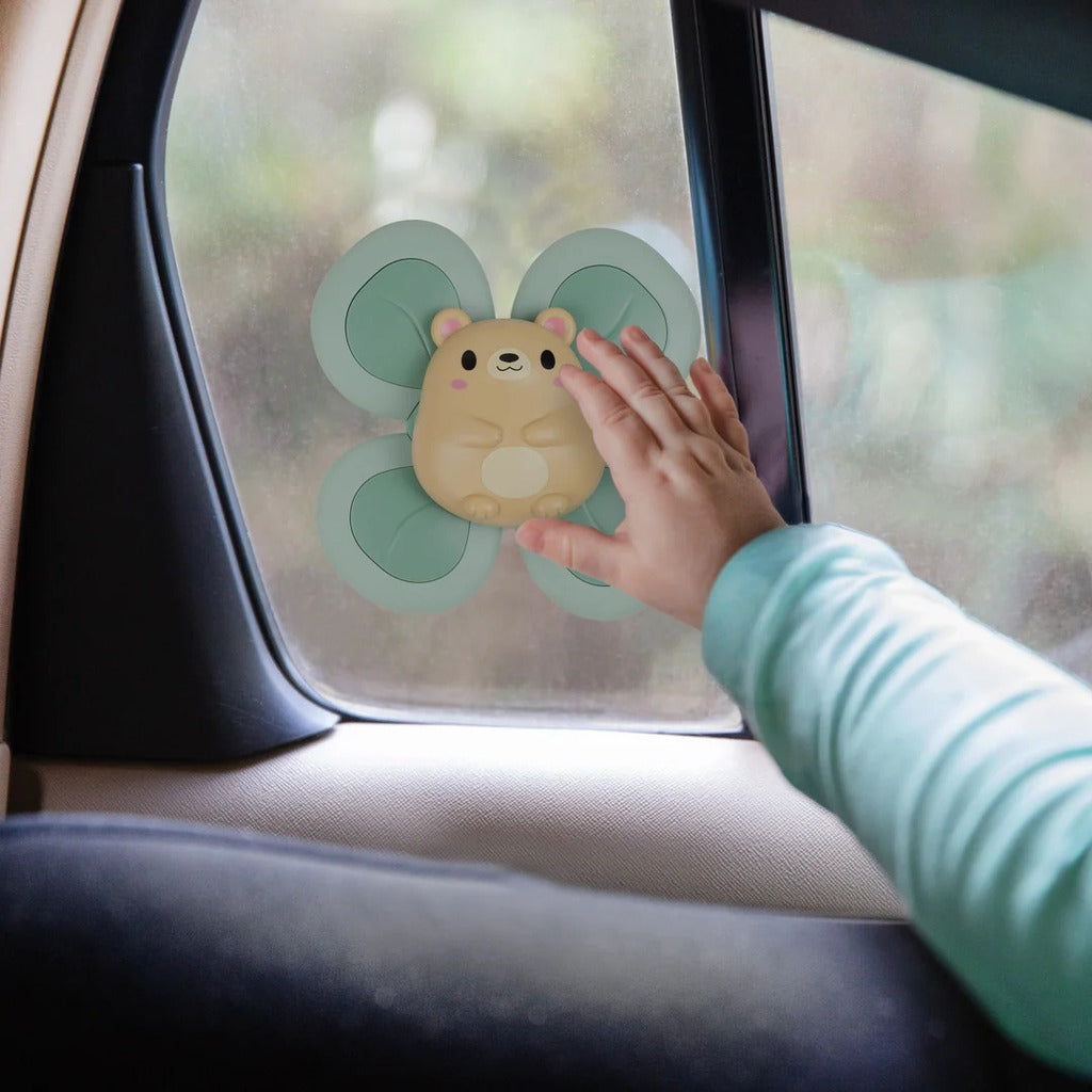 Sensory spinner suctioned to a window with a baby reaching out to turn the patterned disc