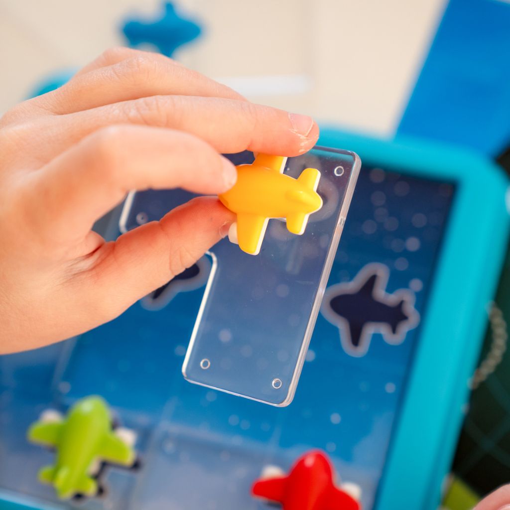 Child placing airplane pieces on the Take Off board while solving a logic challenge at the table