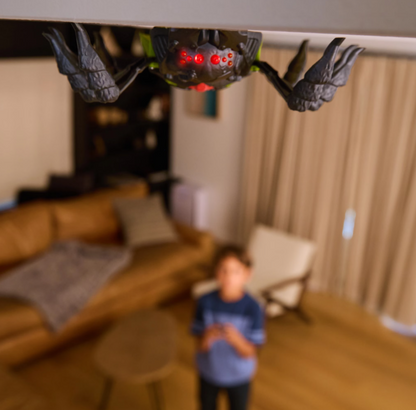 Child steering the spider robot across polished floorboards in a hallway using the handset