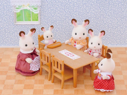 Toy figurines of rabbits around a table in a room with wallpaper and window.