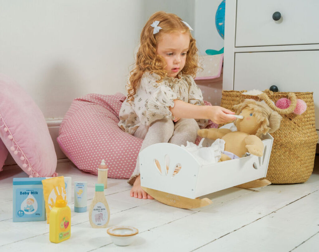 Child feeding a doll with the wooden bottle, with the rest of the set nearby