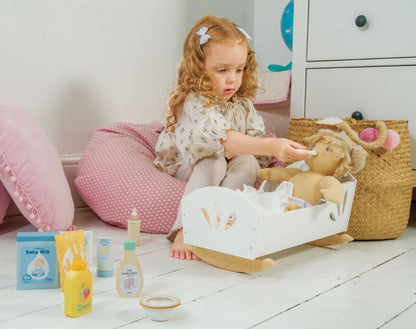 Child feeding a doll with the wooden bottle, with the rest of the set nearby