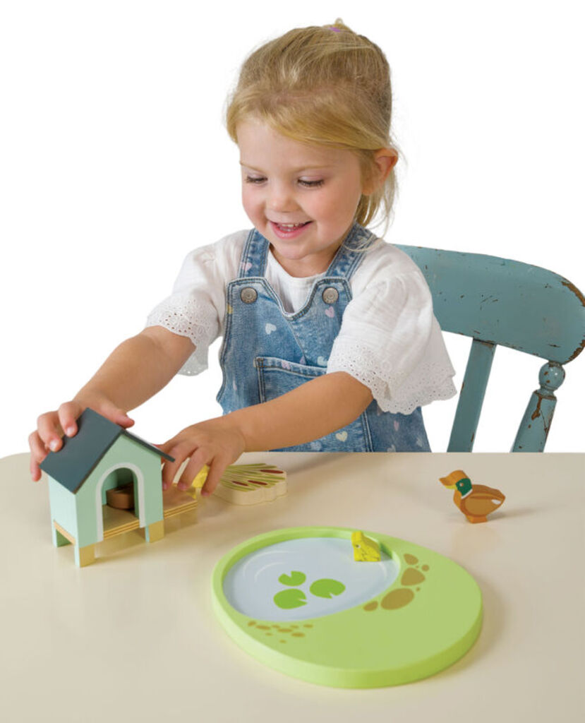 Child arranging the ducklings around the pond set beside a wooden dolls house