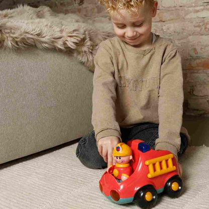 Young child playing indoors with a red toy fire engine featuring a removable firefighter figure, yellow ladder and chunky black wheels.