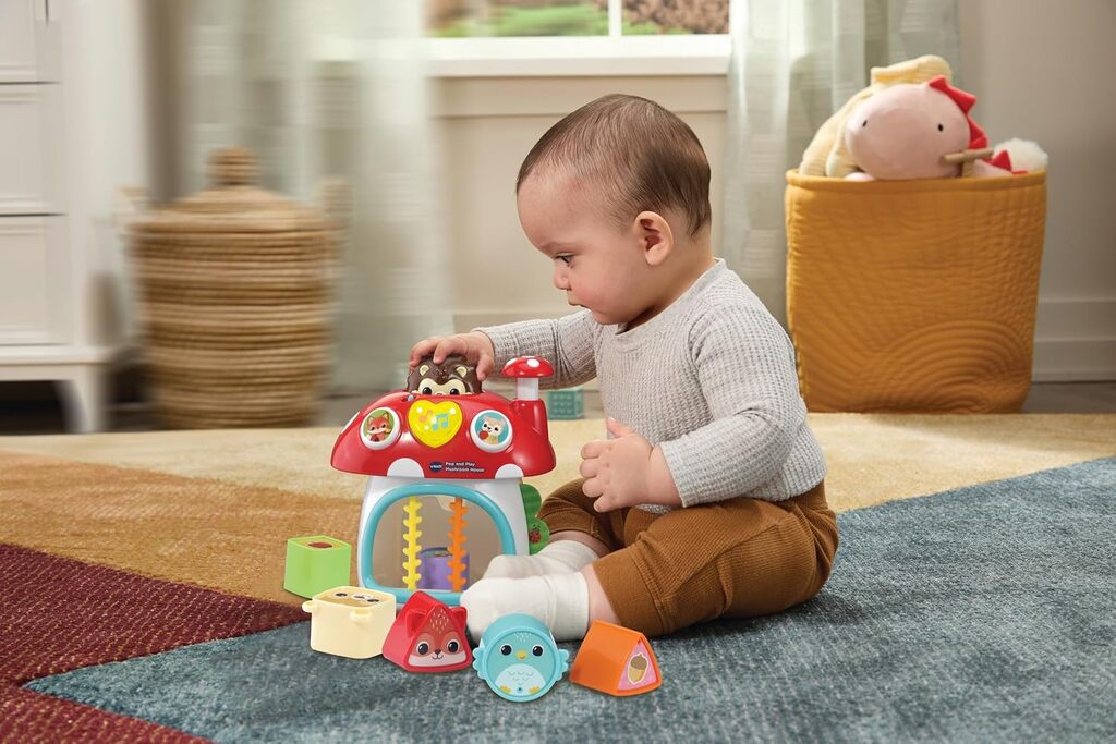Baby sitting on the floor posting a shape block into the Pop and Play Mushroom House