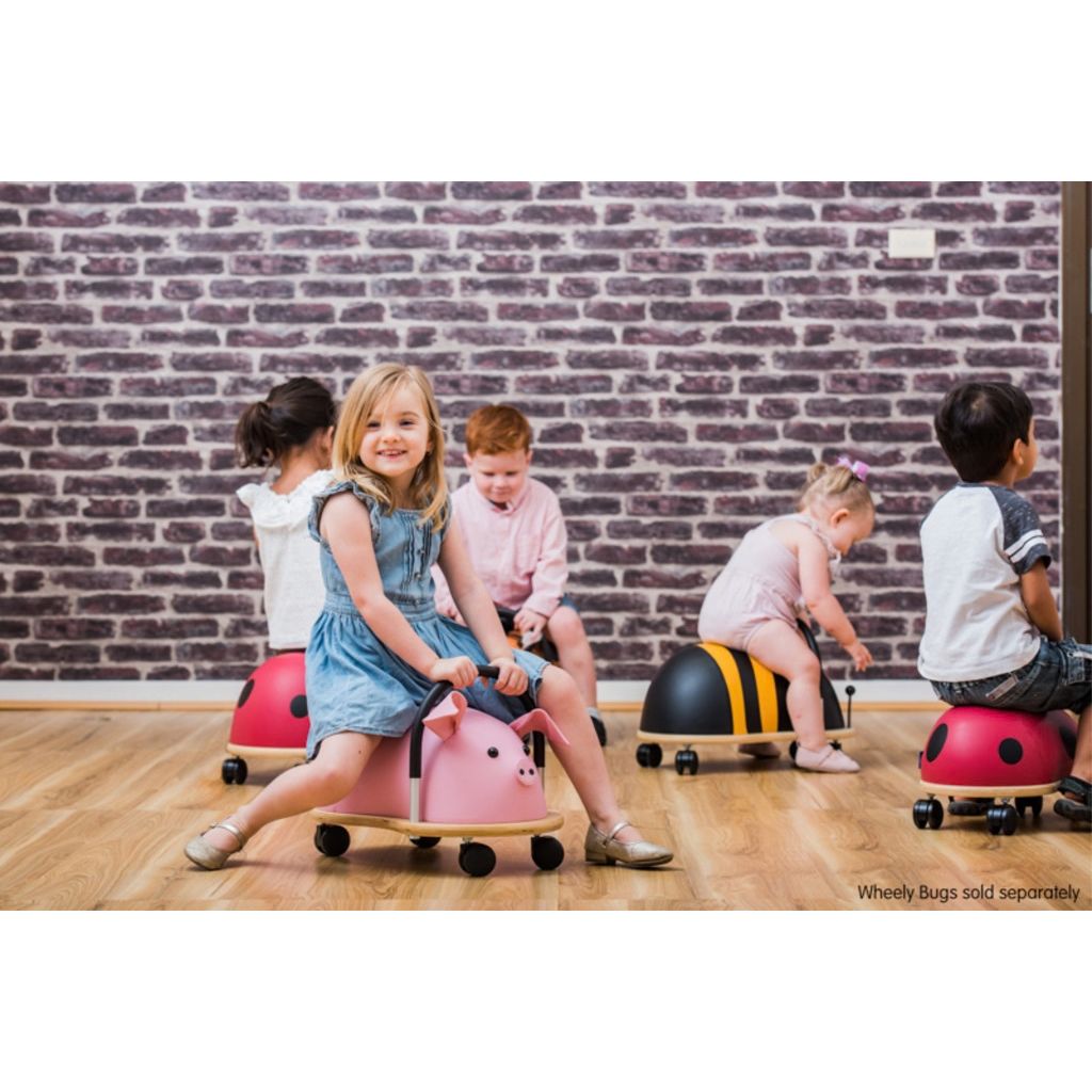 Preschooler riding the Wheely Bug large bee across the floor, building gross motor skills