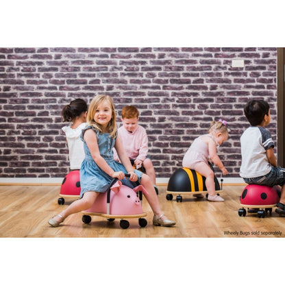 Preschooler riding the Wheely Bug large bee across the floor, building gross motor skills